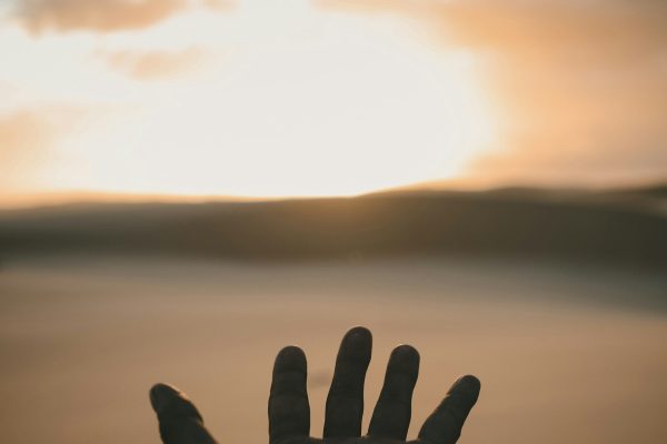 hand reaching out over ocean at Sunset